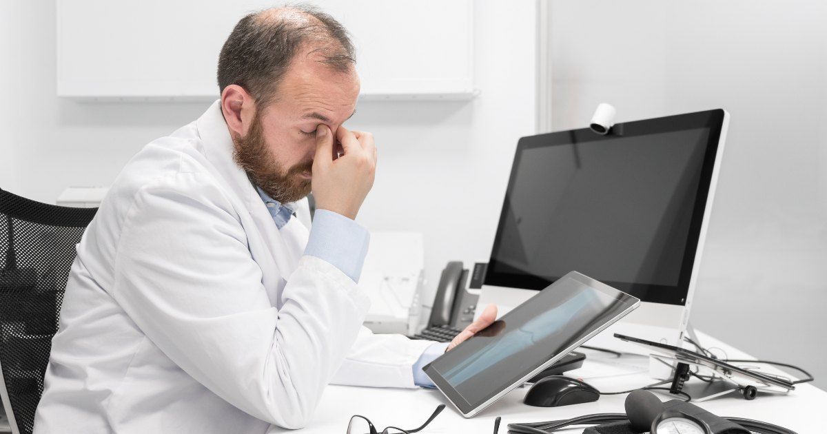 doctor sitting at desk seeming stressed while viewing scans 